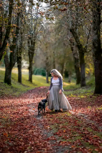Elske walking a small dog along an oak-lined country lane carpeted with autumn leaves, the perfect scene for fall travel in France.
