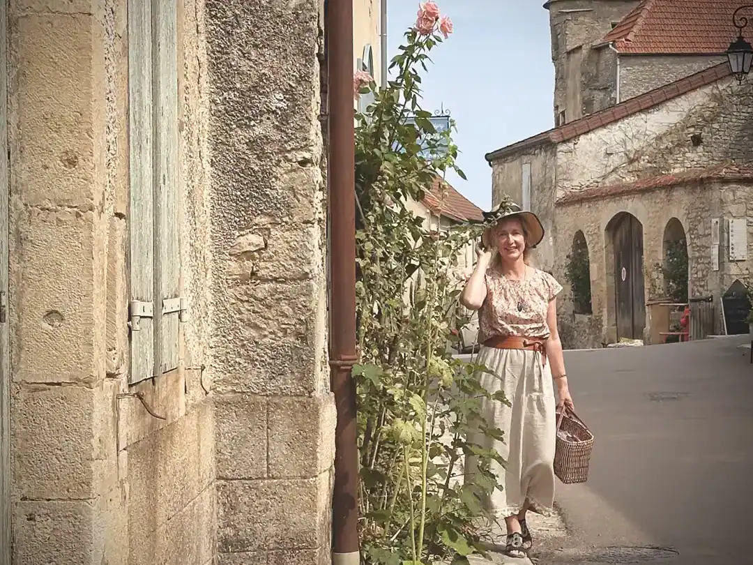 Elske, the author is standing beside an old stone building wearing a sunhat in one of the most beautiful towns in France, Flavigny-sur-Ozerain
